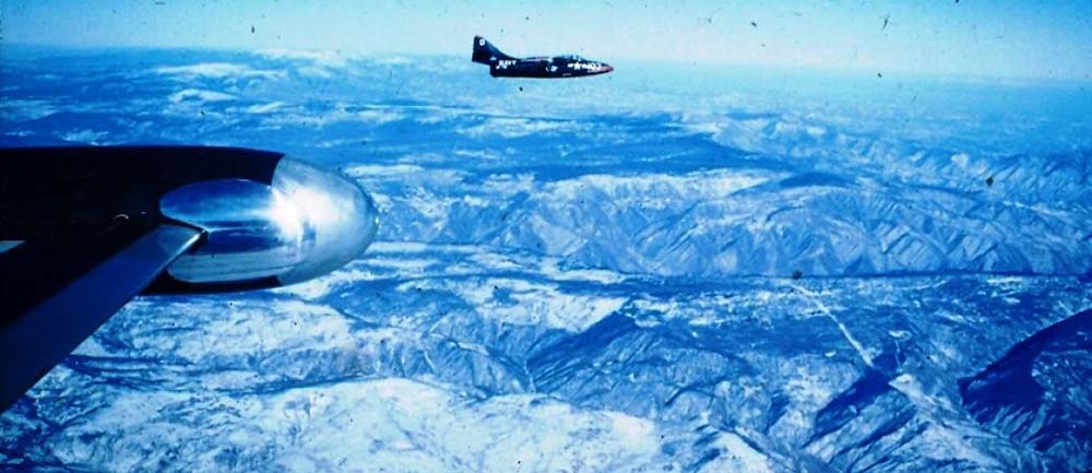 Two Navy F9F aircraft flying over snow covered mountains.
